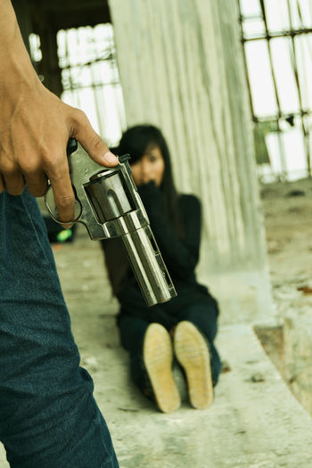 Midsection of man holding gun by hostage woman in abandoned building