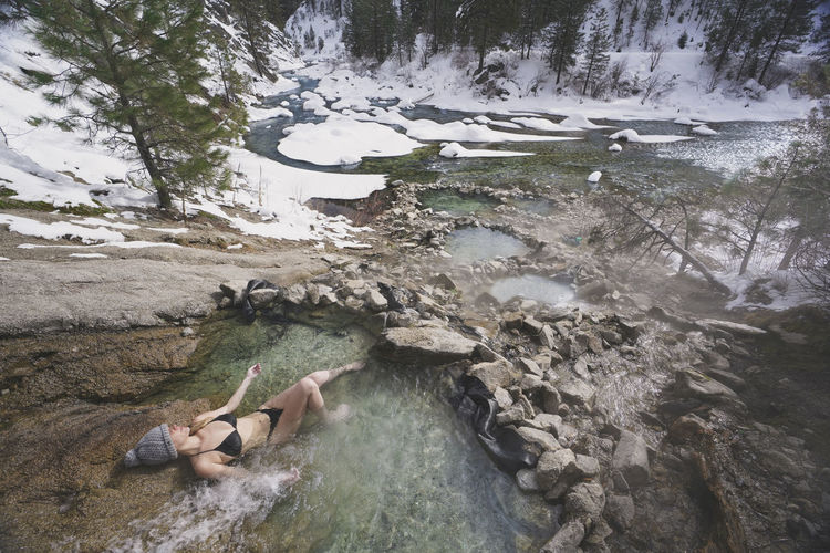 High angle view of woman wearing bikini while relaxing in thermal pool at forest during winter