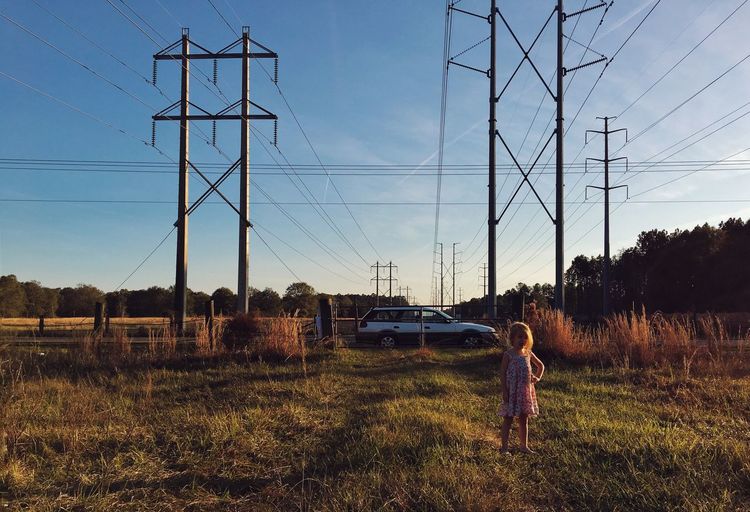 Girl standing on grassy field against electricity pylon