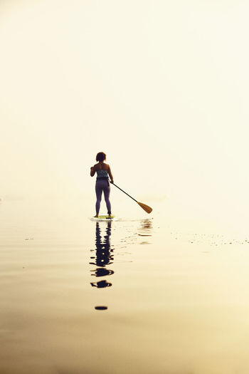Young woman standup paddle boarding on a foggy morning at sunrise