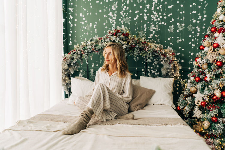 Young beautiful blonde woman in pajamas sits on the bed on a festive christmas morning.