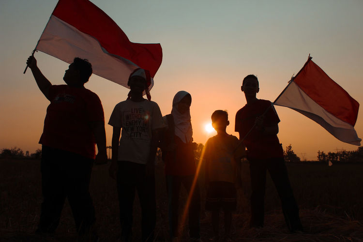 People holding flags against sky during sunset