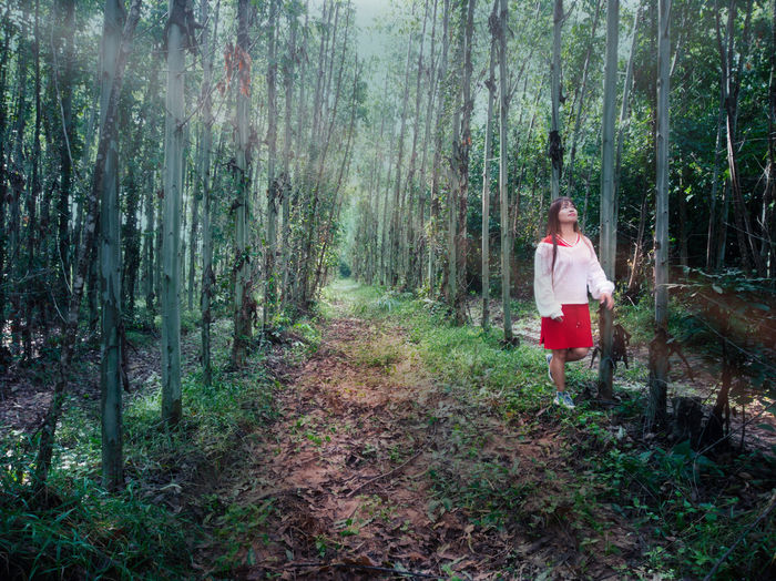 Full length of mid adult woman walking on field amidst trees in forest