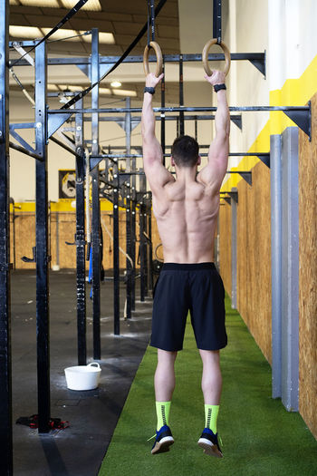 Rear view of fit man training with rings at gym