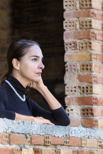 Portrait of a young woman looking away against brick wall