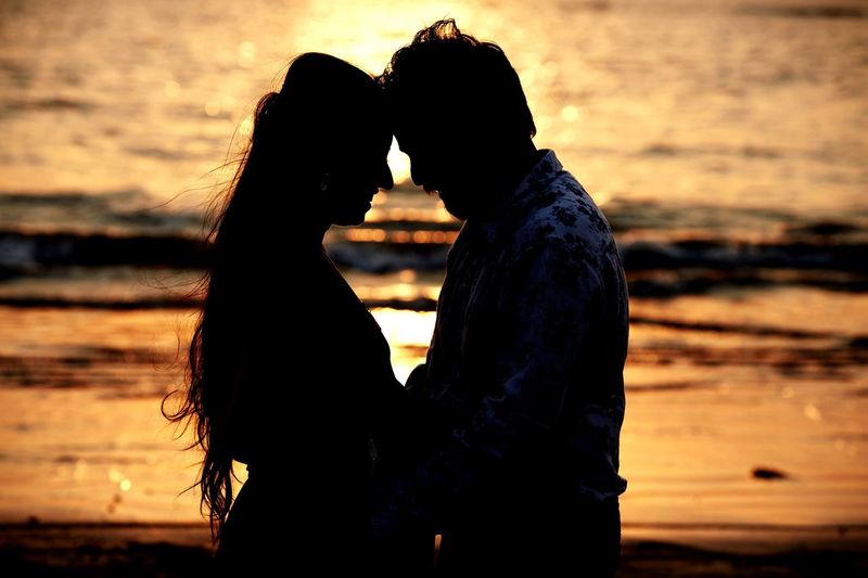 Silhouette couple standing at sea shore during sunset
