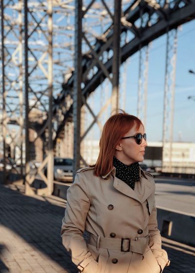 Young woman wearing sunglasses standing against bridge