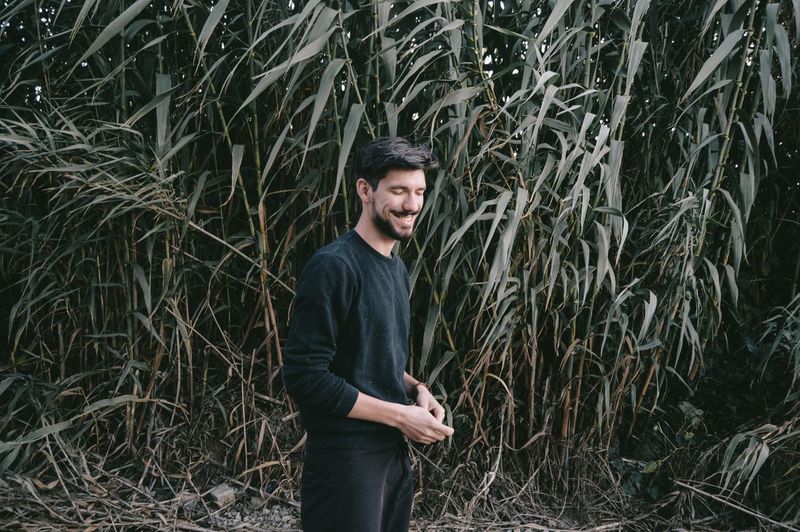 Smiling young man standing against plants on field