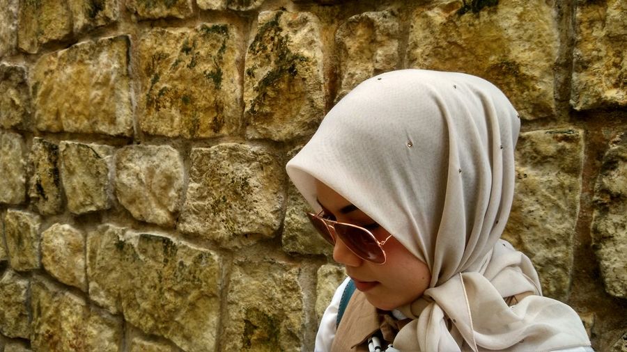 Close-up of woman in sunglasses standing by stone wall