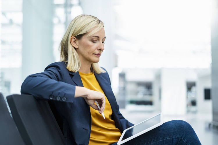 Mature businesswoman using tablet pc sitting on chair in lobby