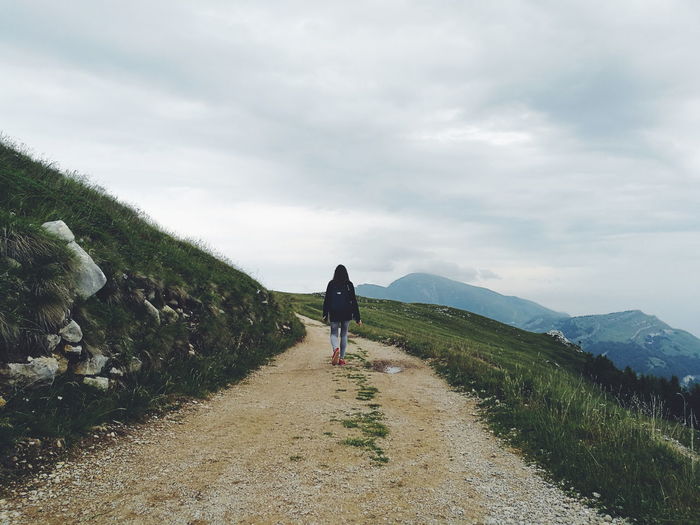 Rear view of woman walking on footpath by mountains against sky