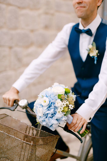 Midsection of groom with bouquet on bicycle outdoors