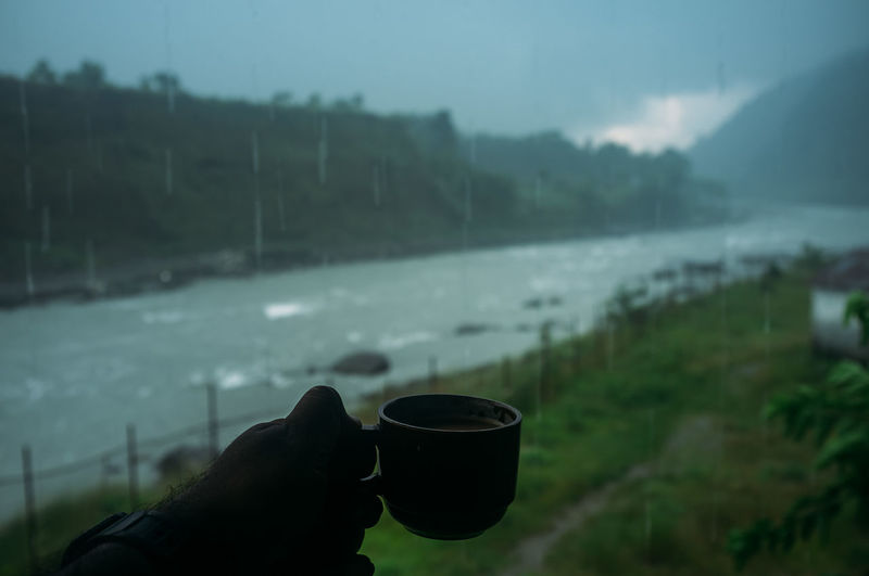 Person holding coffee cup against mountain