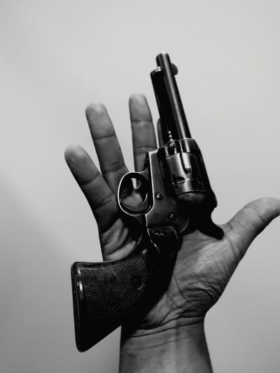 Cropped hand of man holding gun against white background