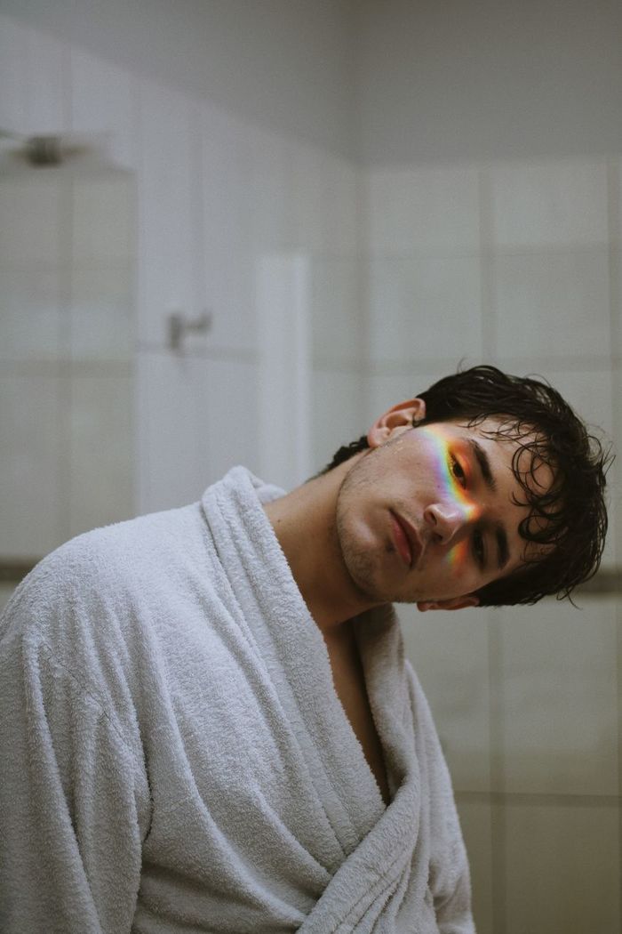 Prism light falling on face of thoughtful young man standing in bathroom
