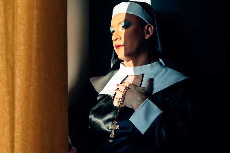 Devoted nun prays in the light of a convent window. cross dressing drag queen, religion, identity.