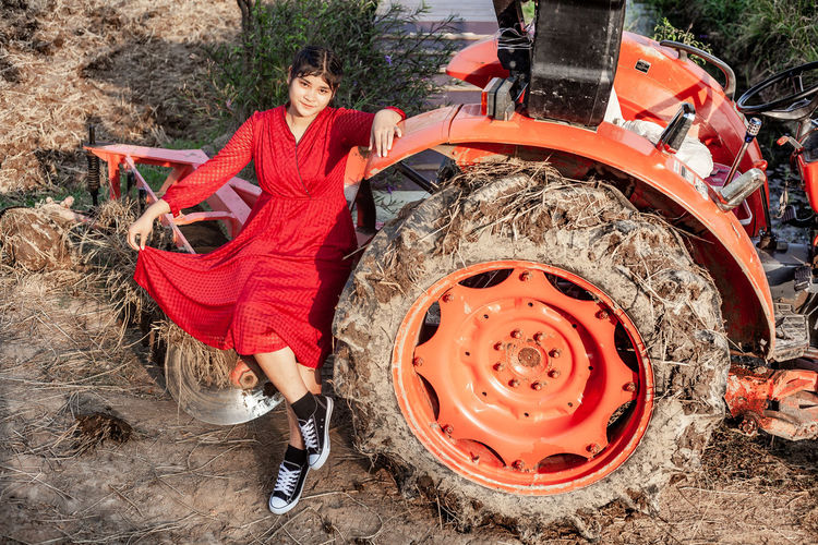 Portrait of happiness pretty beautiful chubby girl with red dress posing with orange tractor.