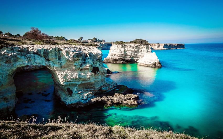 Idyllic shot of rock formation in sea at salento against sky