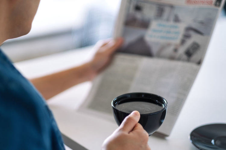 Cropped image of man having coffee while reading newspaper at table
