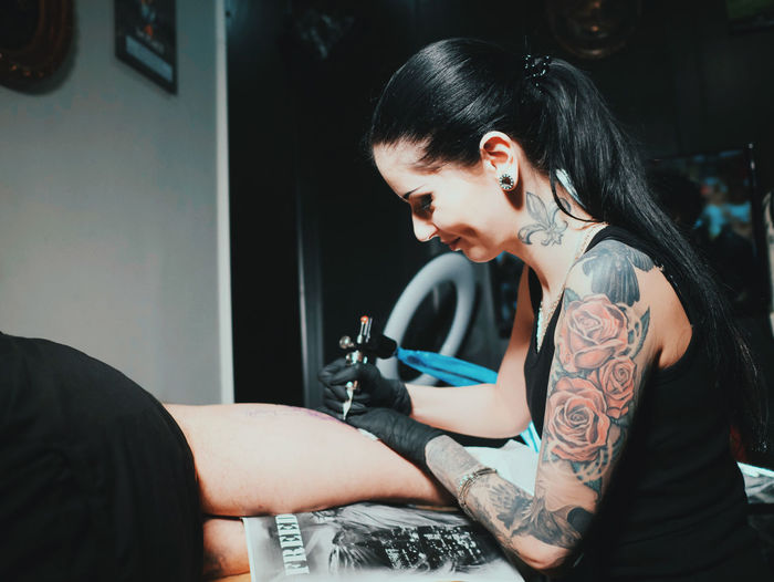 Young woman tattooing statue of liberty man on calf at parlor
