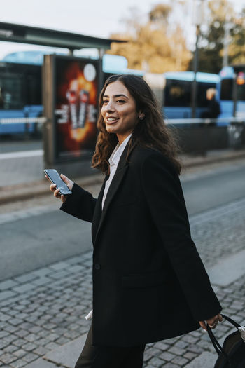 Side view of a smiling young woman using phone in city