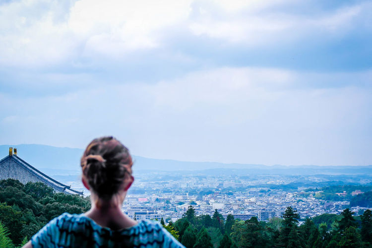 Rear view of woman looking at cityscape against cloudy sky