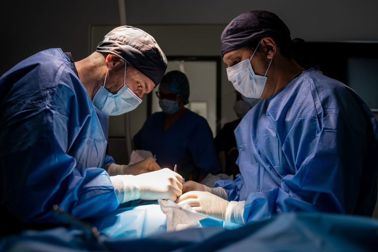 Surgeons and nurses in uniform concentrating and operating patient using special equipment in operating room of contemporary hospital