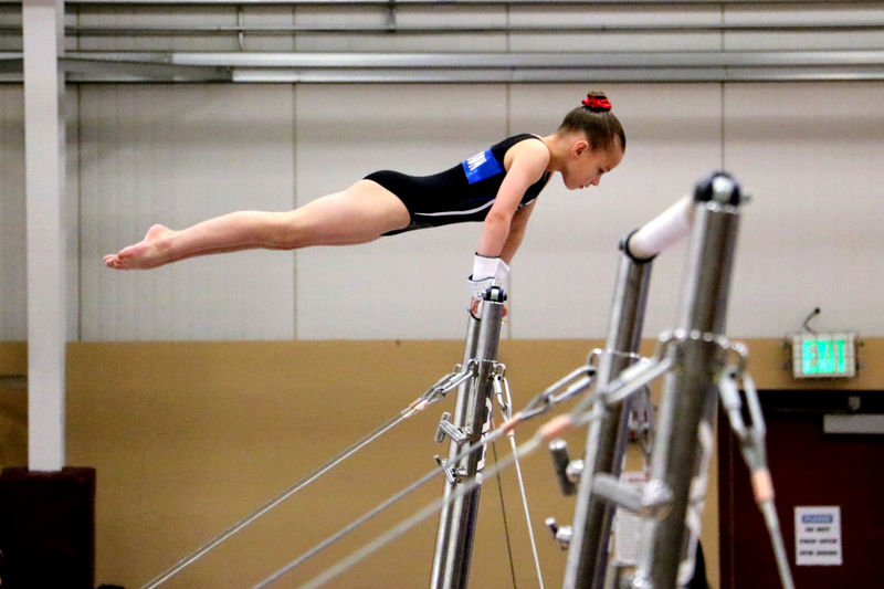 Side view of gymnast girl exercising on bars in gym