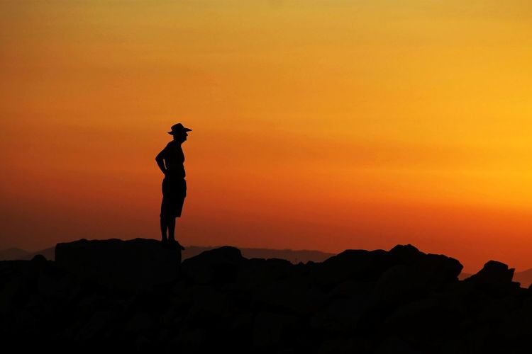 Silhouette man standing on rock against orange sky
