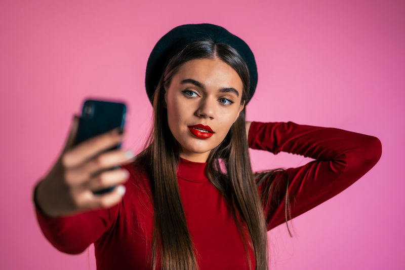 Portrait of beautiful young woman using smart phone against pink background