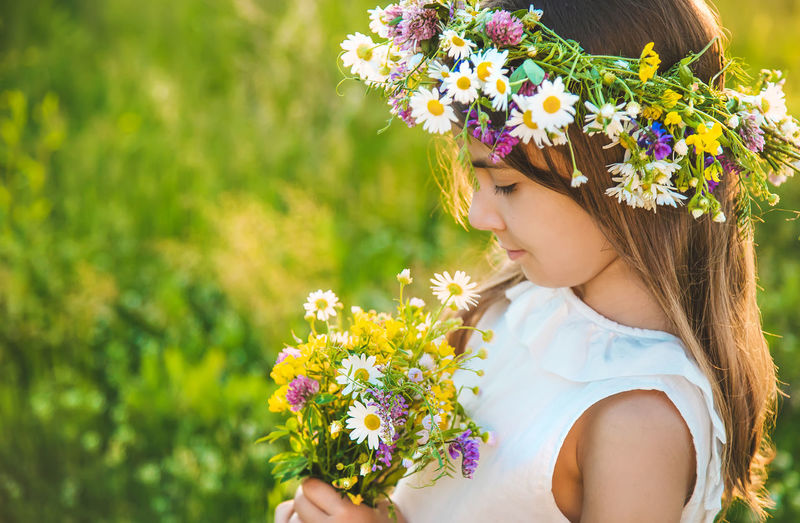 Side view of girl wearing floral crown holding flowers