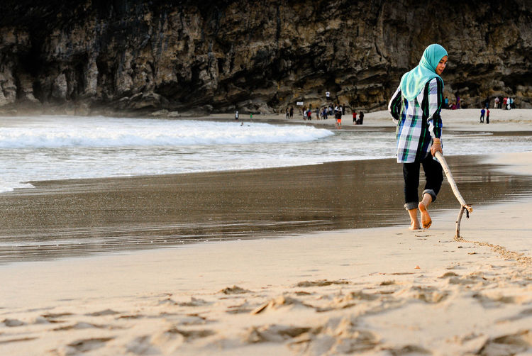 Woman in hijab playing with driftwood at beach