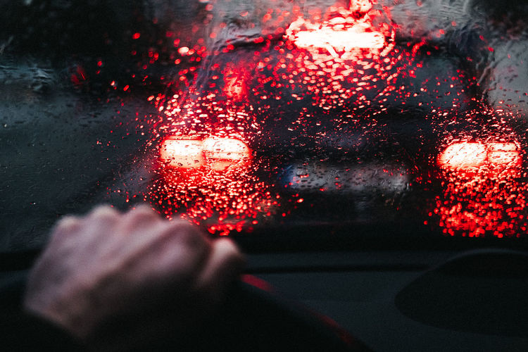 Person seen through wet car windshield during rainy season