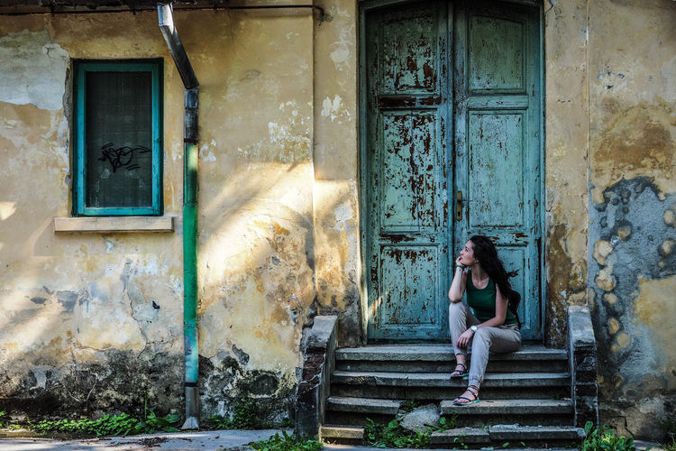 Full length of young woman sitting against abandoned house