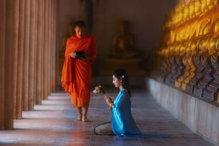 Side view of woman praying while monk walking in buddhist temple