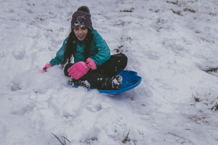 Full length of girl sitting on bobsled in snow