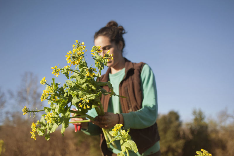 Woman examining plants in field against clear blue sky