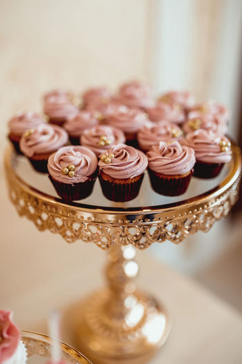 Cupcakes with pink cream and decorated with golden pastry beads on a golden tray 