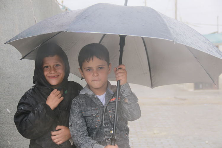 Portrait of boy with umbrella standing in rain