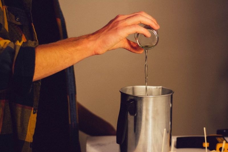 Midsection of person pouring liquid wax in pitcher