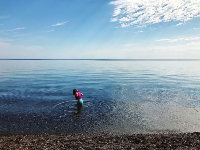 Girl standing in sea against blue sky