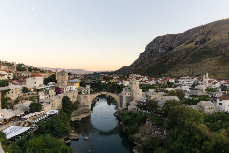 Stari most over river neretva in city against clear sky during sunset