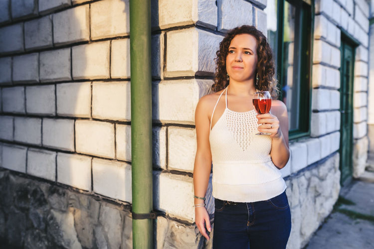 Woman having red wine against house