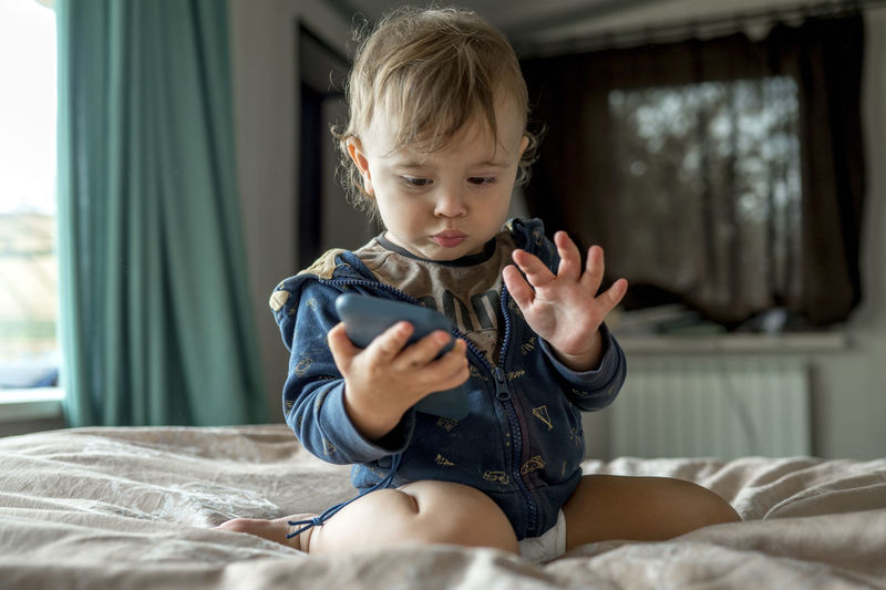 Cute baby boy looking at mobile phone on bed
