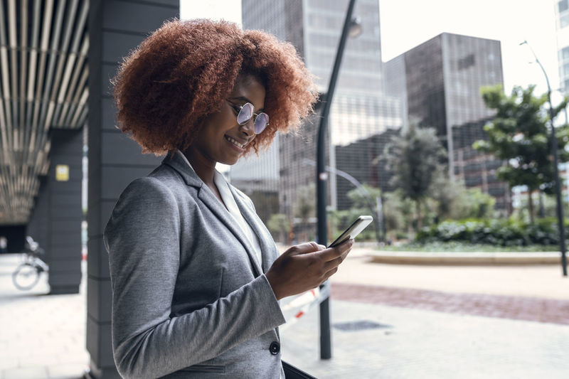 Young businesswoman smiling while using smart phone outdoors