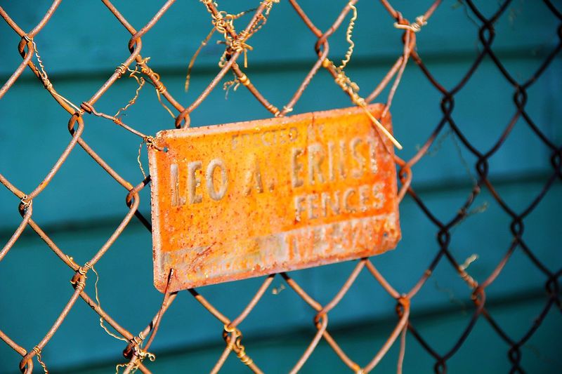 Close-up of text over chainlink fence against sky