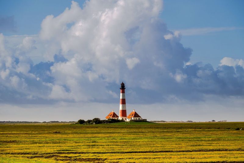 Lighthouse on grassy field against cloudy sky