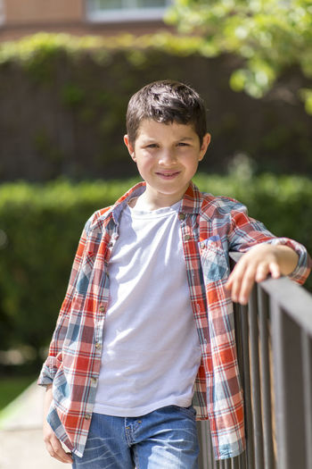 Portrait of boy standing by railing at park