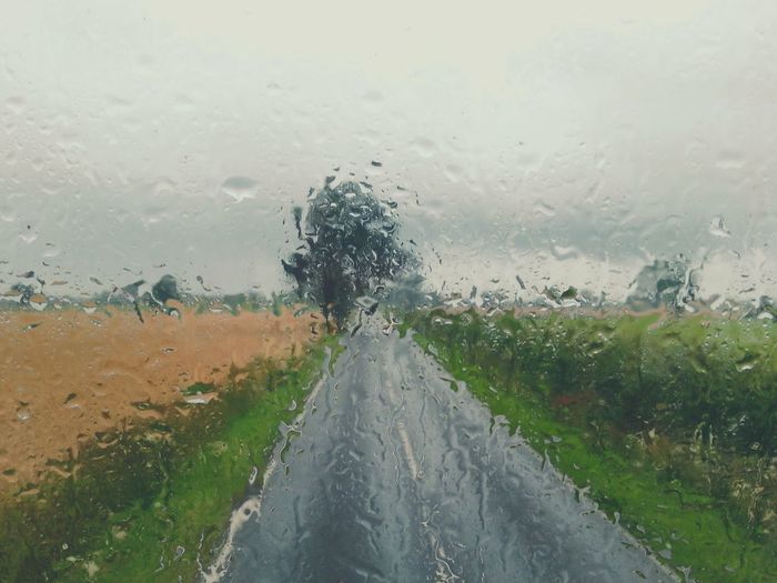 Rain drops on road against cloudy sky
