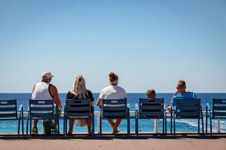 Rear view of family sitting on chairs at beach against clear blue sky